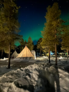 tipi i skogen under en norrskenshimmel